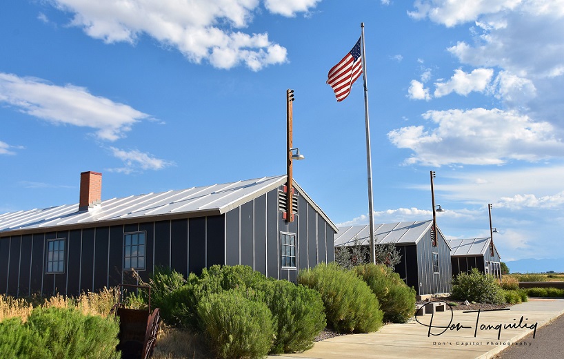 Photo of the Heart Mountain Interpretive Center three building and an American flag on a pole with blue skies and clouds. Visit Powell