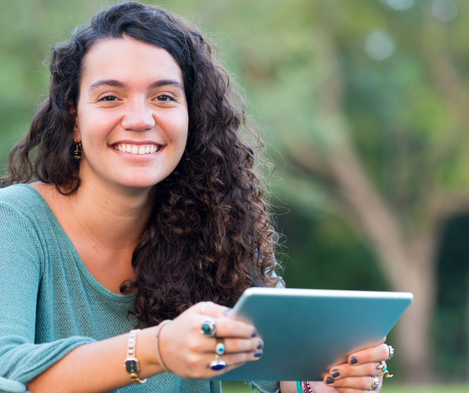 Northwest College student outdoors smiling. She has long curly dark hair and a green three quarter length shirt. she is wearing a watch and a bunch of rings.