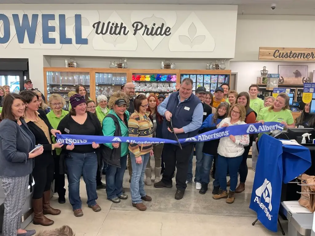John (JW) Wesen, store manager for the new Albertsons in Powell, Wyoming cutting the ceremonial ribbon surrounded by a crowd of people holding the ribbon
