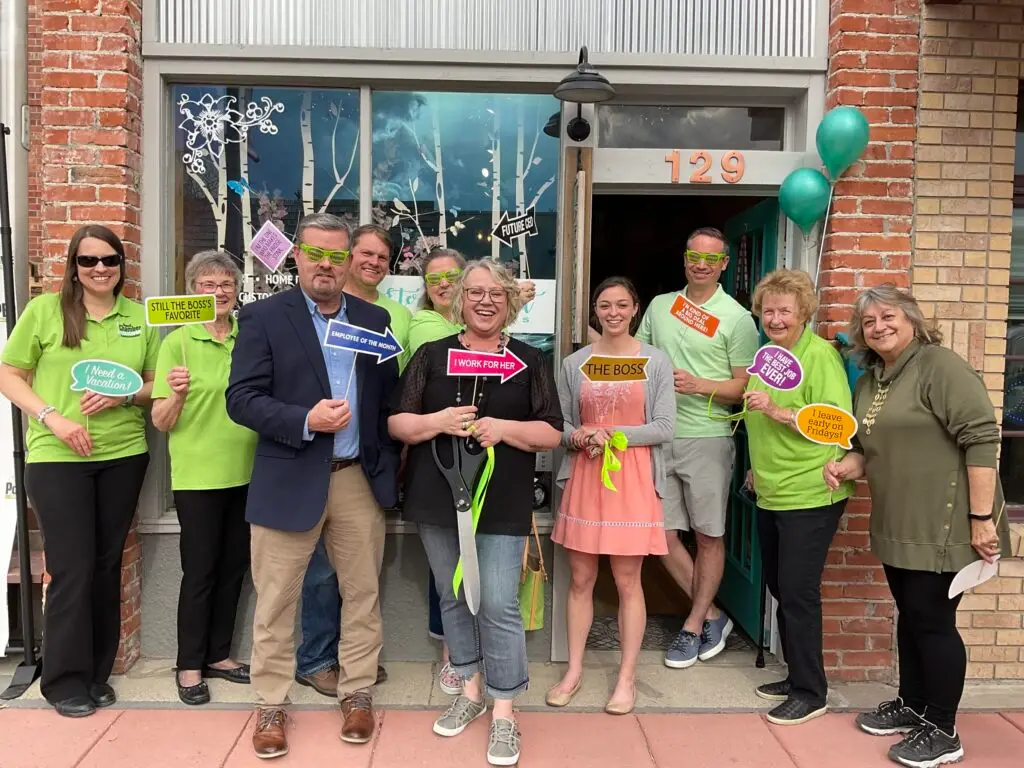 Powell Chamber of Commerce staff members and ambassadors posing at a ribbon cutting ceremony, holding humorous work-related props