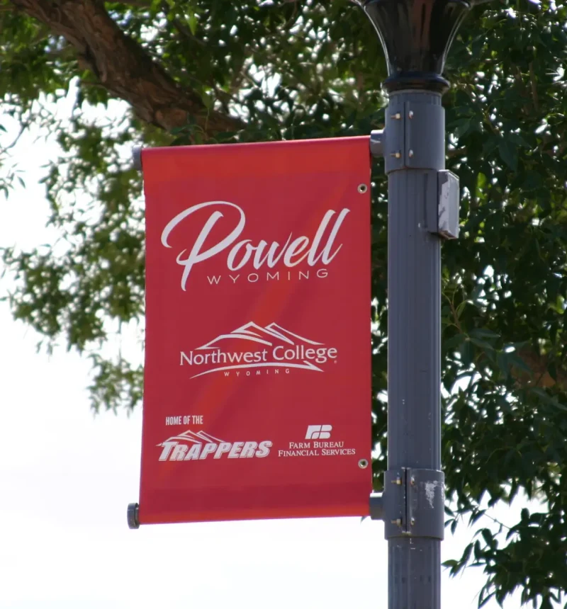 A promotional sponsor banner in downtown Powell, Wyoming featuring Northwest College, Northwest College Athletics, and Farm Bureau Financial Services