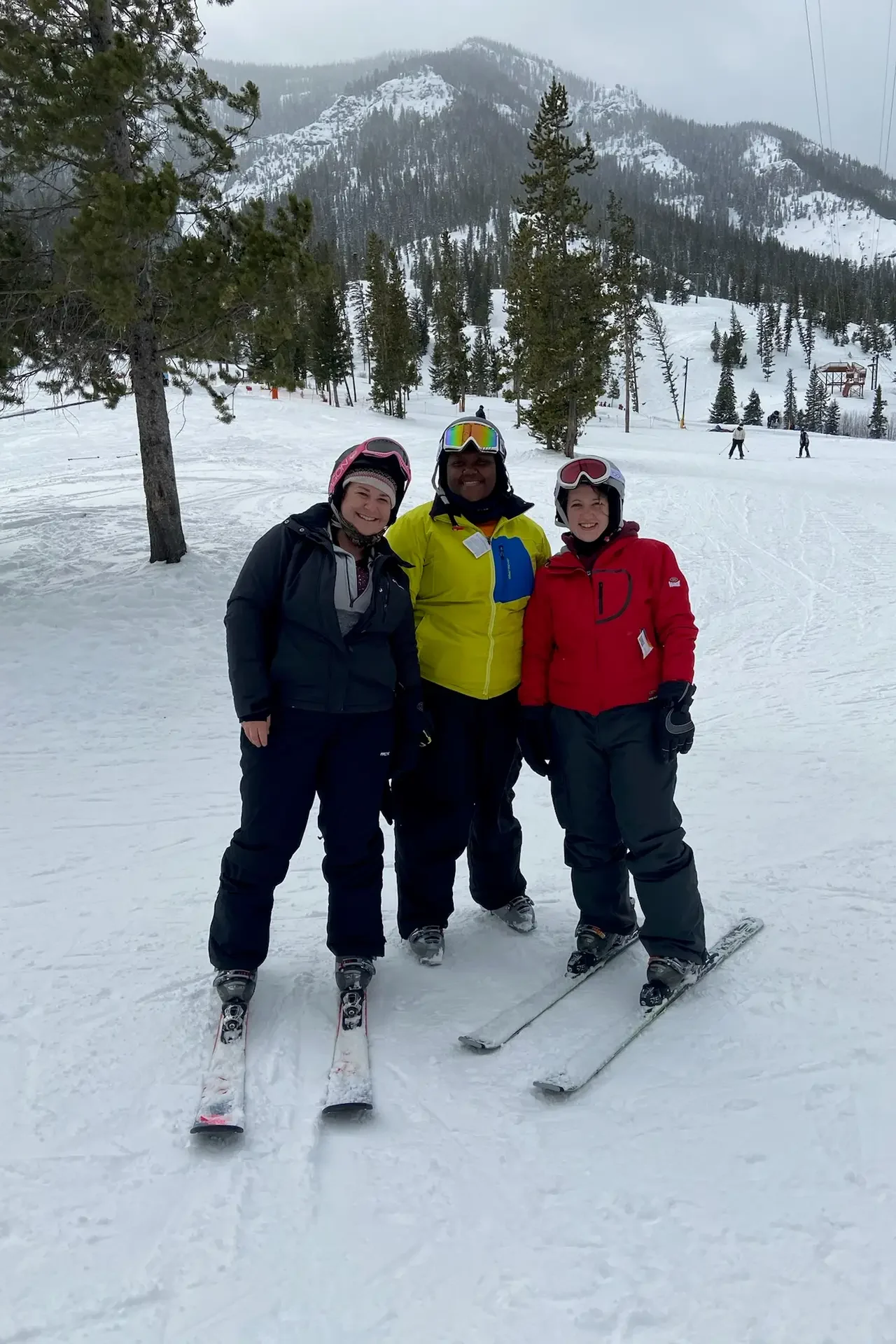 A group of three young women smiling atop a snowy mountain in skis