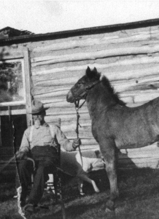 Peter McCulloch sitting in a rocking chair and holding onto the halter of a foal in front of his home in Worden, Montana